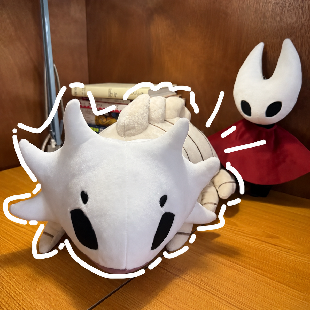 Bell Beast plush on a wooden tabletop with a red-cloaked figure in the background