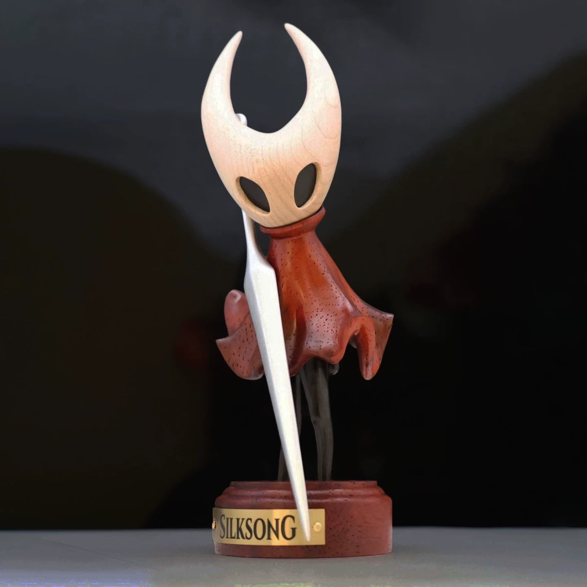 Hornet wooden figure on a Silksong display base against a dark background